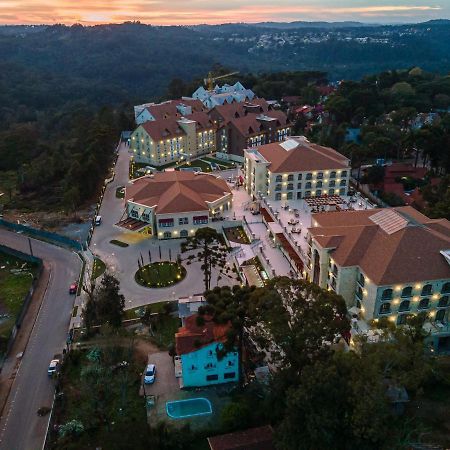 Buona Vitta Gramado Resort & Spa By Gramado Parks Экстерьер фото The photo shows an aerial view of a hotel complex set in a hilly, wooded area. The buildings feature a mix of architectural styles with several structures, including a central round pavilion. Surrounding the buildings are well-maintained gardens and 