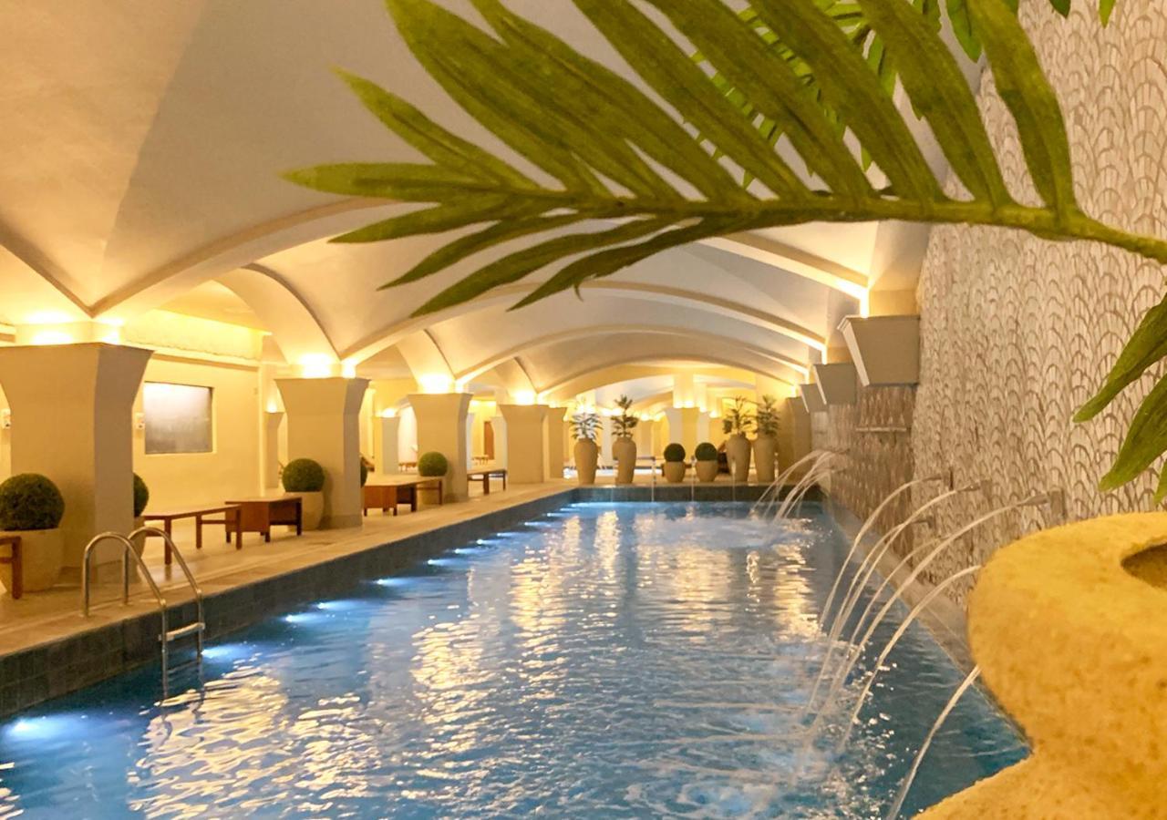 Buona Vitta Gramado Resort & Spa By Gramado Parks Экстерьер фото The photo shows an indoor swimming pool with a serene and elegant atmosphere. The pool has a calm blue water surface, illuminated by soft lights along its edges. The architectural design features arches in the ceiling, creating an open and spacious f