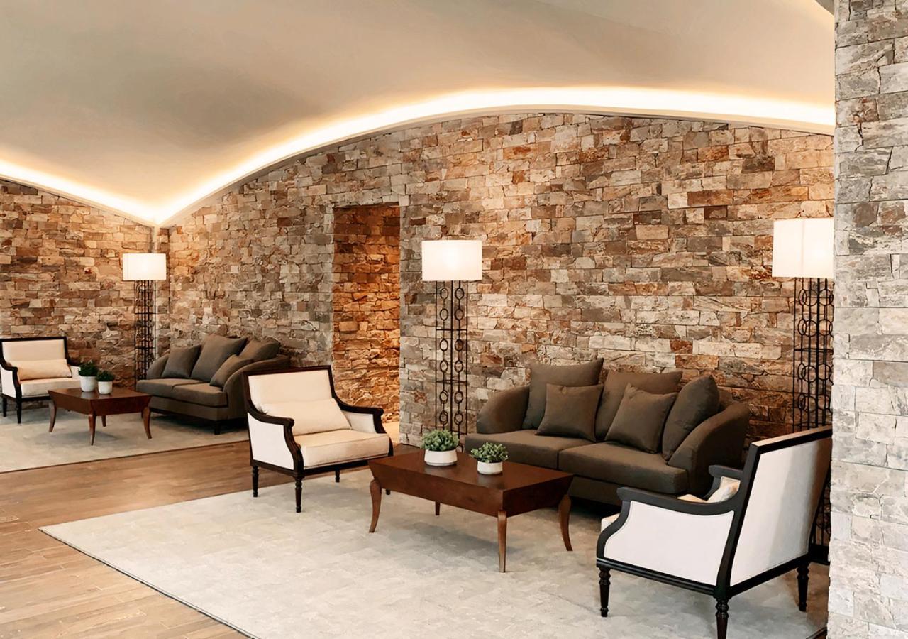 Buona Vitta Gramado Resort & Spa By Gramado Parks Экстерьер фото The photo shows a stylish and modern lounge area. The walls are made of natural stone, creating a warm and inviting atmosphere. There are two comfortable sofas in a muted gray color arranged around a wooden coffee table. Flanking the sofas are elegan