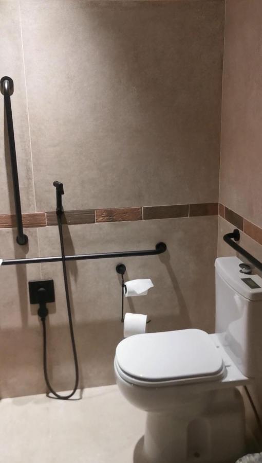 Buona Vitta Gramado Resort & Spa By Gramado Parks Экстерьер фото The photo shows a bathroom equipped with grab bars for accessibility. The walls are tiled in a neutral color, and there is a toilet on the right side of the image. Two rolls of toilet paper are positioned near the toilet, and there are additional ins