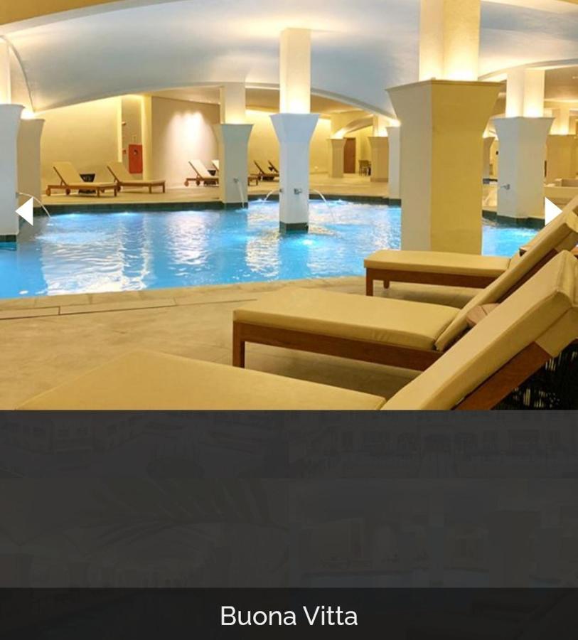 Buona Vitta Gramado Resort & Spa By Gramado Parks Экстерьер фото The photo shows a tranquil indoor pool area, featuring a large swimming pool with clear blue water. Surrounding the pool are several lounge chairs made of light-colored wood, positioned for relaxation. The space is well-lit, with soft lighting highli