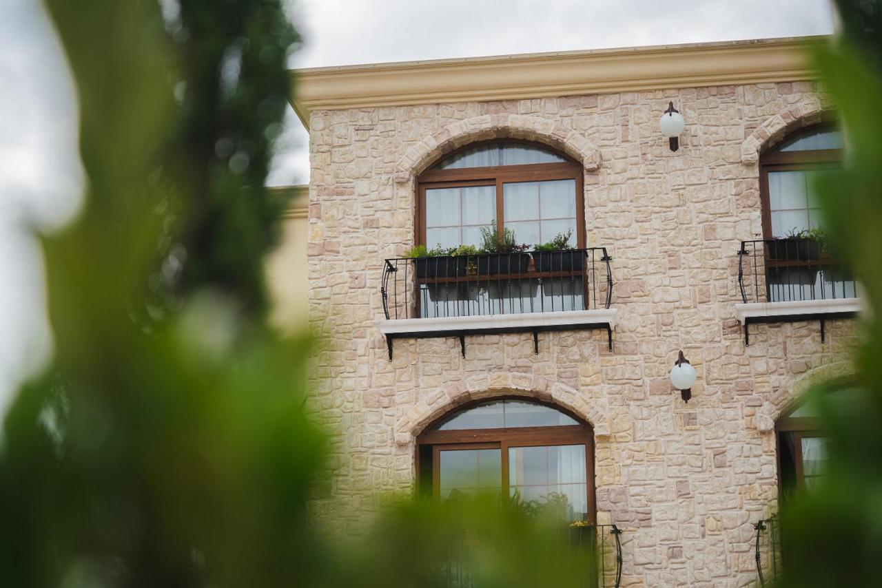 Buona Vitta Gramado Resort & Spa By Gramado Parks Экстерьер фото The photo depicts a stone building with a textured exterior. It features several windows with wooden frames. Each window has a small balcony adorned with decorative plants. There are also wall-mounted light fixtures flanking the windows. In the foreg