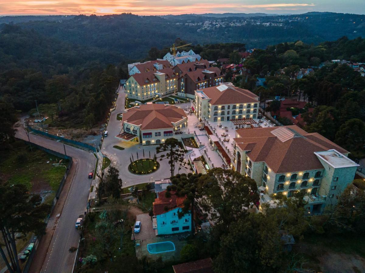Buona Vitta Gramado Resort & Spa By Gramado Parks Экстерьер фото The photo shows an aerial view of a hotel complex set in a hilly, wooded area. The buildings feature a mix of architectural styles with several structures, including a central round pavilion. Surrounding the buildings are well-maintained gardens and 