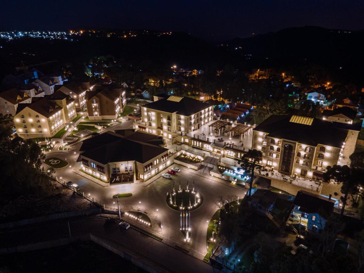 Buona Vitta Gramado Resort & Spa By Gramado Parks Экстерьер фото The photo shows a beautifully lit resort or hotel complex taken at night. The buildings are well-illuminated, highlighting their architecture. There is a circular area with a fountain at the center, surrounded by pathways that connect various parts o