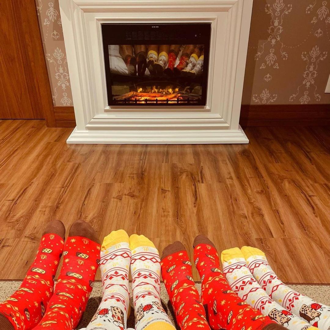 Buona Vitta Gramado Resort & Spa By Gramado Parks Экстерьер фото The photo shows a cozy indoor setting with a warm fireplace. In the foreground, several pairs of feet are displayed, each wearing brightly colored socks with various patterns. The socks include red, yellow, and white designs, contributing to a cheerf