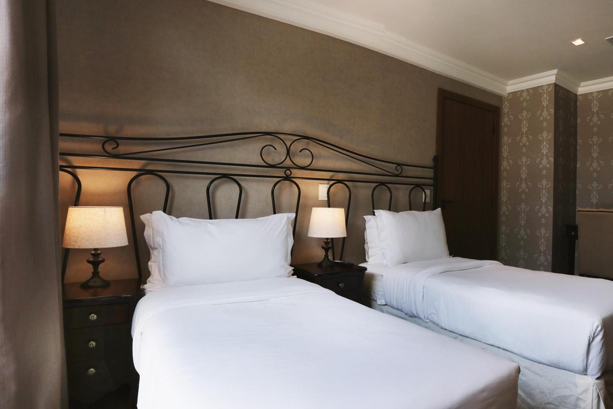 Buona Vitta Gramado Resort & Spa By Gramado Parks Экстерьер фото The photo shows a neatly arranged hotel room featuring two single beds with white bedding. The beds have decorative metal headboards, and there are bedside tables on either side with lamps. The room's walls have a subtle design, and there is a door v