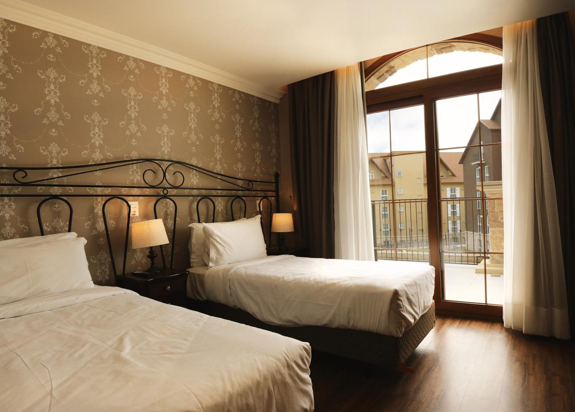 Buona Vitta Gramado Resort & Spa By Gramado Parks Экстерьер фото The photo shows a well-decorated hotel room featuring two beds. One bed is larger, likely a double bed, while the other is a single bed. The walls are adorned with a floral pattern, and there are bedside lamps next to the larger bed. Large windows wi