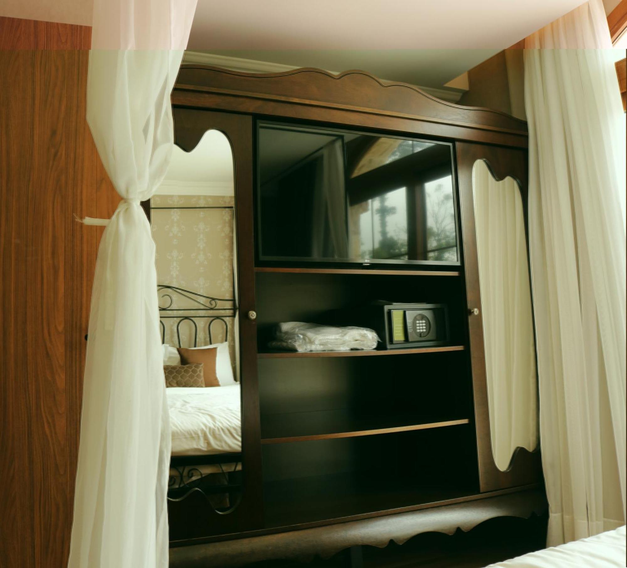 Buona Vitta Gramado Resort & Spa By Gramado Parks Экстерьер фото The image shows a wooden cabinet with a television mounted on the front. The cabinet has decorative edges and is paired with sheer white curtains on either side. Inside the cabinet, there are shelves, and a small safe or storage box is visible on one