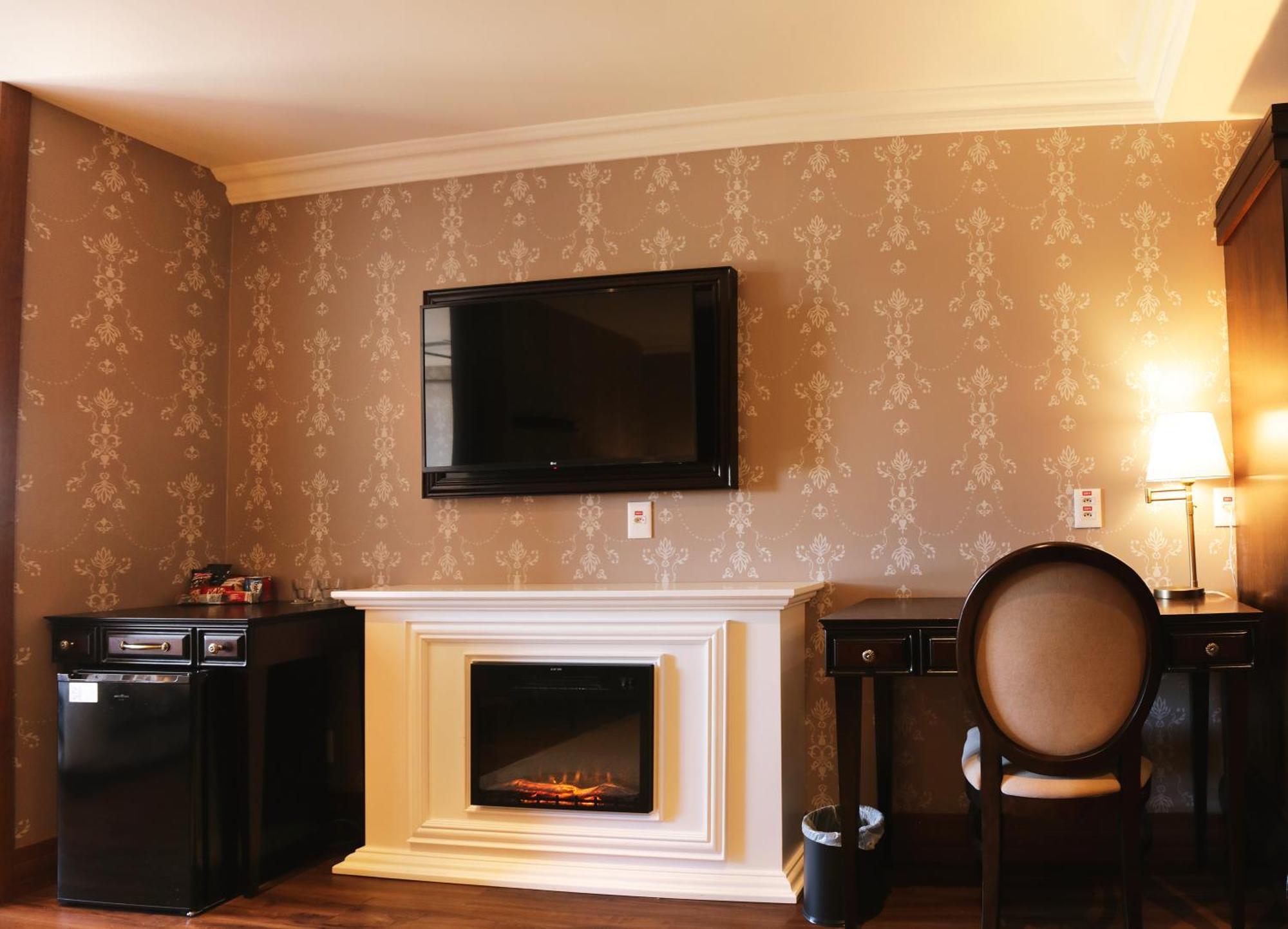 Buona Vitta Gramado Resort & Spa By Gramado Parks Экстерьер фото The photo shows a cozy room featuring a decorative wall with a subtle pattern. On one side, there is a modern flat-screen television mounted on the wall. Below it, there is a stylish electric fireplace framed in white. Adjacent to the fireplace is a 