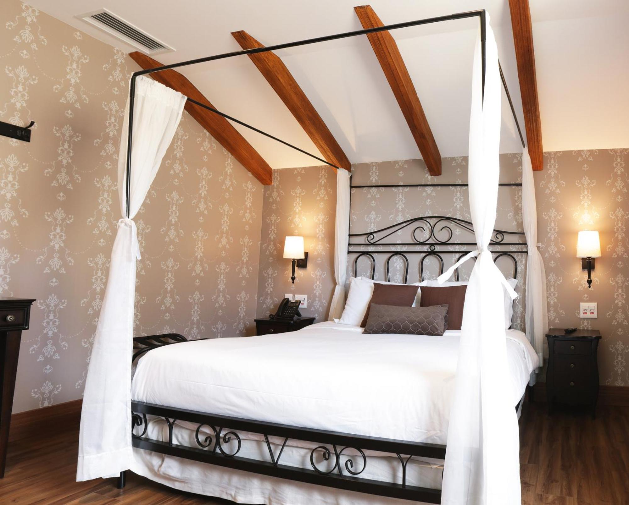 Buona Vitta Gramado Resort & Spa By Gramado Parks Экстерьер фото The photo shows a beautifully designed bedroom featuring a four-poster bed with a metal frame and flowing white curtains. The bed is adorned with white bedding and brown decorative pillows. The room has wooden beams on the ceiling and is decorated wi