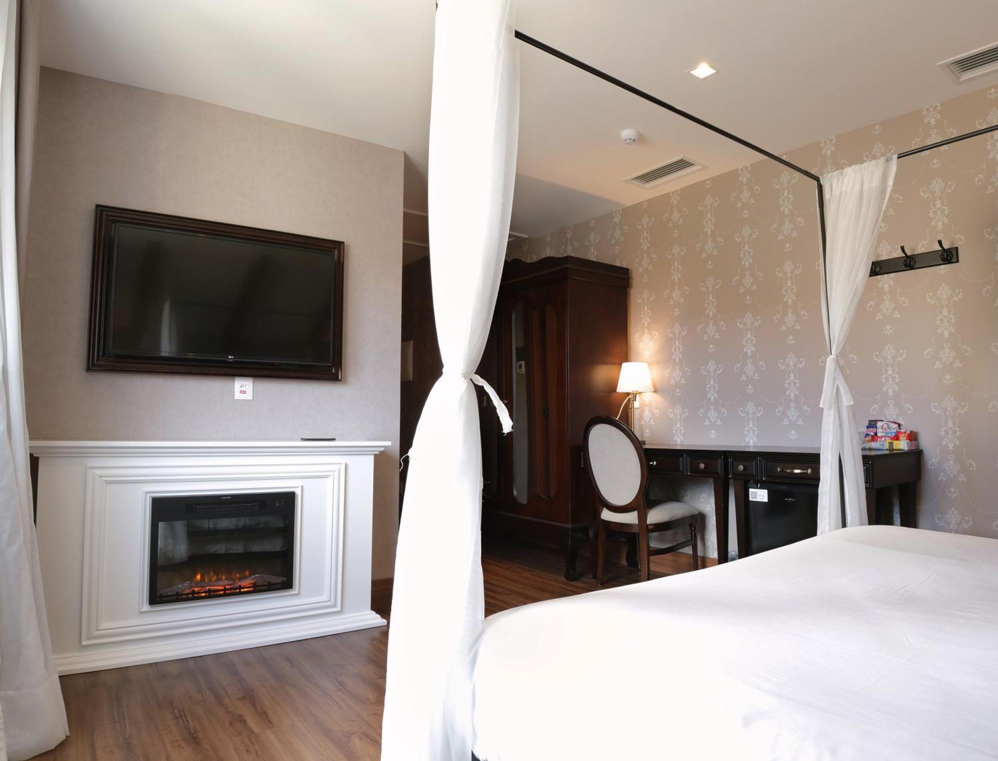 Buona Vitta Gramado Resort & Spa By Gramado Parks Экстерьер фото The photo shows a cozy hotel room with elegant decor. There is a white bed with a canopy, and a modern television mounted on the wall across from it. To the side, a fireplace is built into a white mantel, adding a warm touch to the space. There's a w