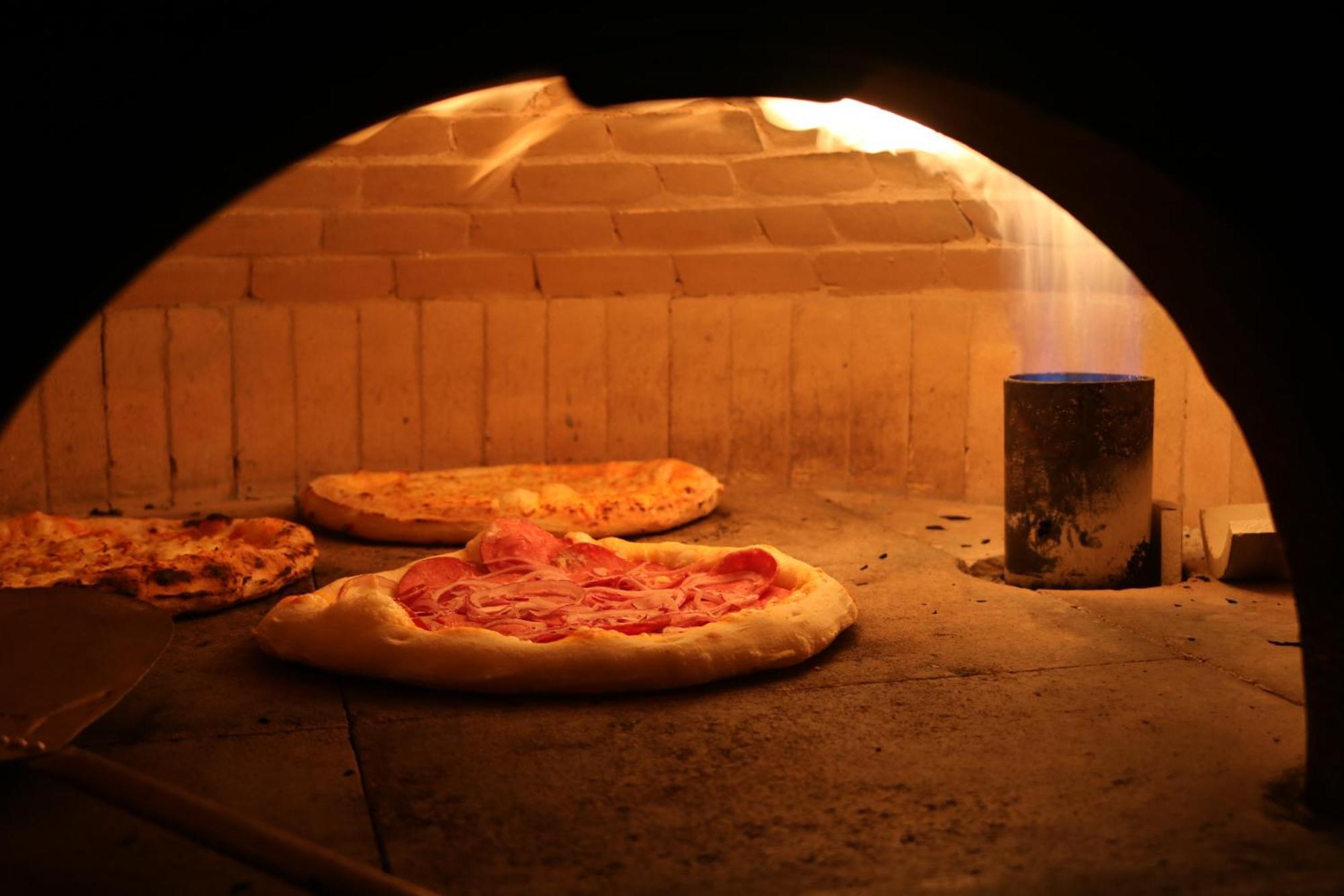 Buona Vitta Gramado Resort & Spa By Gramado Parks Экстерьер фото The photo shows a traditional pizza oven. Inside the oven, there are several pizzas placed on the stone surface. The pizzas appear to have various toppings, including what looks like cheese and possibly pepperoni. The oven has a warm, glowing ambianc