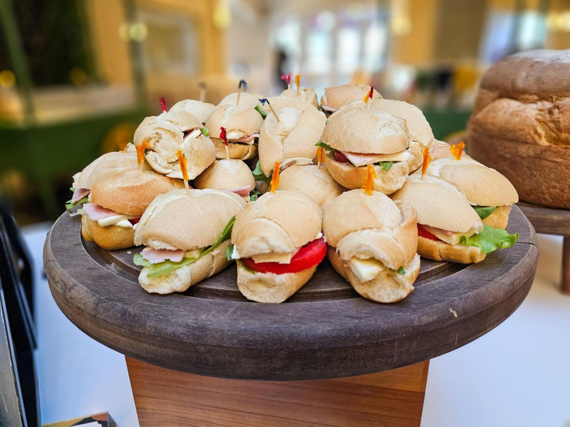 Buona Vitta Gramado Resort & Spa By Gramado Parks Экстерьер фото The photo shows a platter of small sandwiches, likely sliders, arranged neatly on a wooden serving tray. These sandwiches have various fillings, including what appears to be ham, lettuce, and tomato. They are garnished with colorful toothpicks, and t
